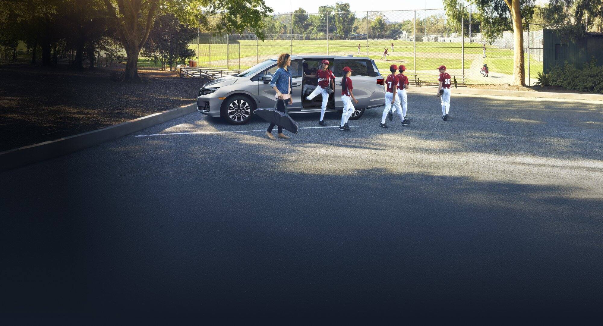 2026 Honda Odyssey Elite in Solar Silver Metallic, parked in parking lot with baseball field in background.