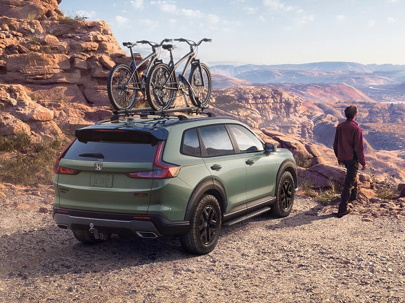 2027 Honda CR-V TrailSport Hybrid in Ash Green Metallic back desert canyon with bikes on roof (Compact Crossover SUV).